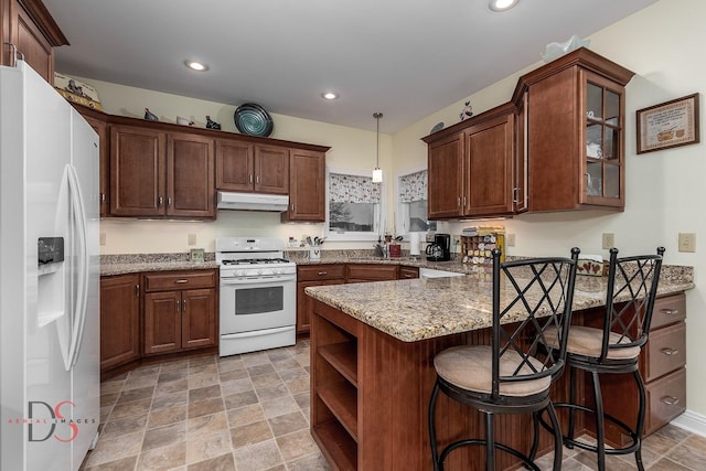 kitchen featuring a breakfast bar area, light stone counters, decorative light fixtures, kitchen peninsula, and white appliances