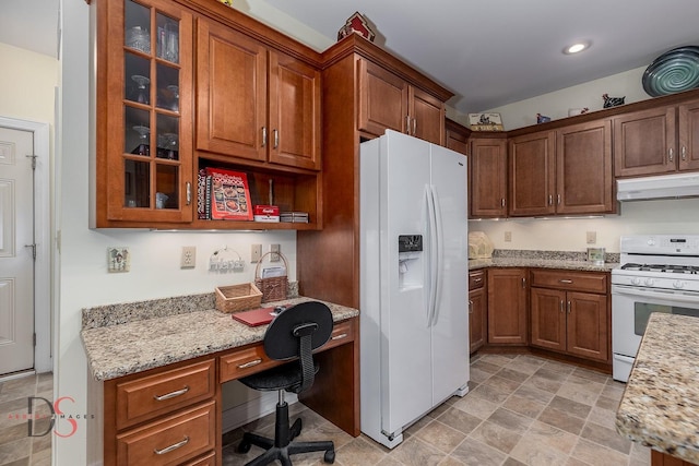 kitchen featuring light stone counters, white appliances, and built in desk