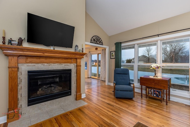 living room featuring high vaulted ceiling, a fireplace, and light wood-type flooring