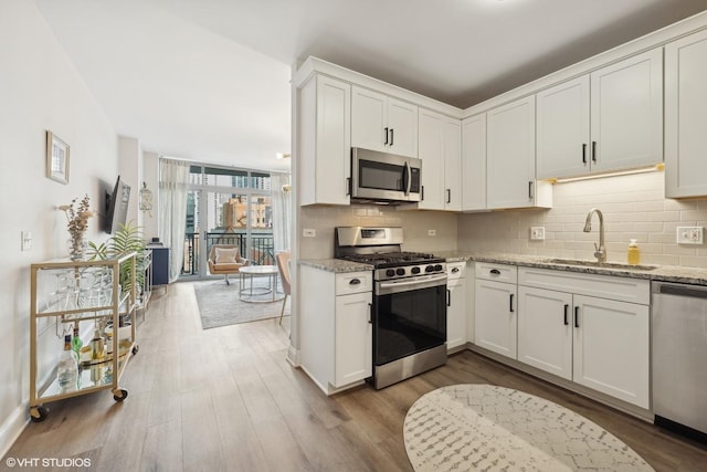 kitchen with appliances with stainless steel finishes, tasteful backsplash, sink, white cabinets, and light stone countertops