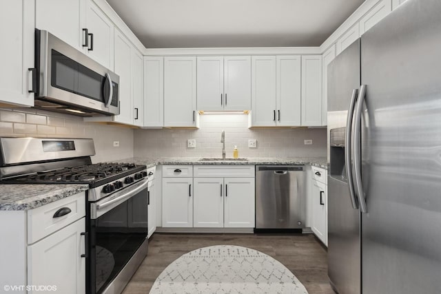 kitchen with sink, light stone countertops, white cabinets, and appliances with stainless steel finishes