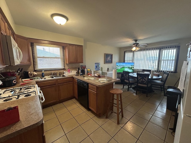 kitchen featuring sink, a breakfast bar area, light tile patterned floors, kitchen peninsula, and white appliances