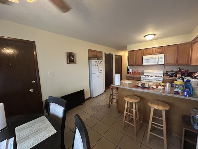 kitchen featuring a kitchen bar, kitchen peninsula, white appliances, tile patterned flooring, and backsplash