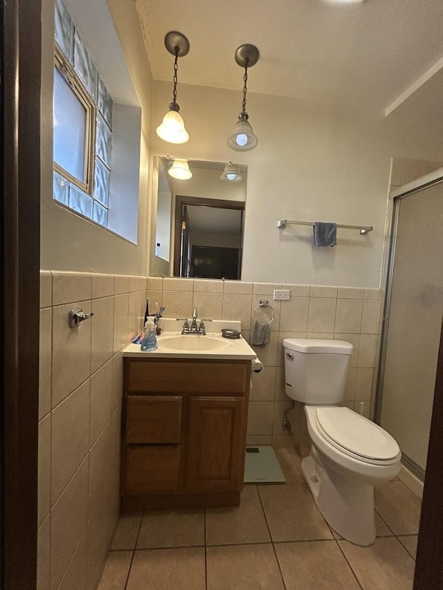 bathroom with tile patterned floors, toilet, tile walls, vanity, and a shower with door