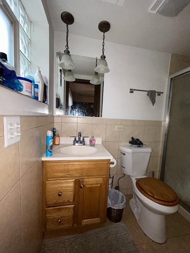 bathroom featuring tile patterned floors, toilet, tile walls, vanity, and a shower with door