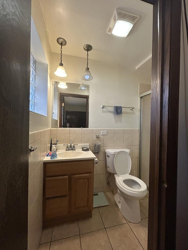 bathroom with tile walls, vanity, toilet, a shower with door, and tile patterned floors