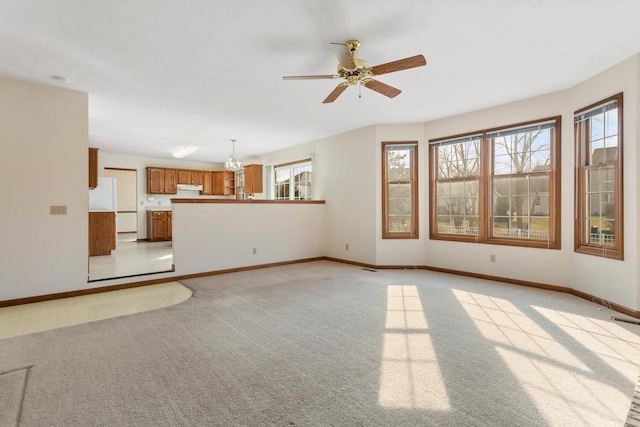 unfurnished living room with baseboards, ceiling fan with notable chandelier, visible vents, and light colored carpet