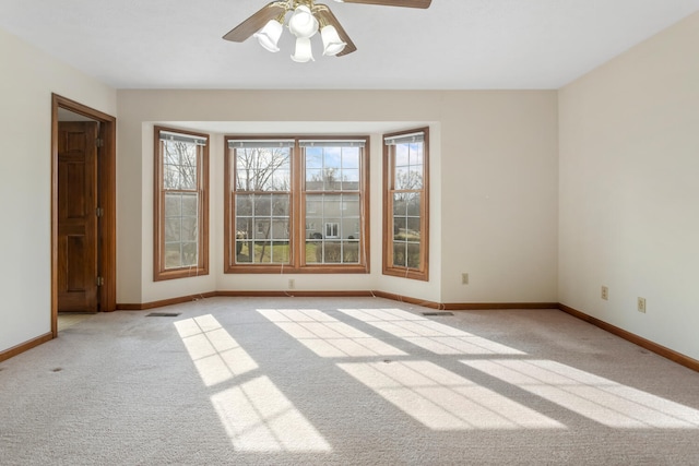 empty room with light colored carpet, ceiling fan, visible vents, and baseboards