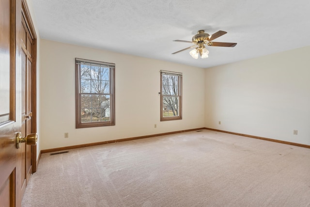 spare room with light carpet, ceiling fan, a textured ceiling, and baseboards