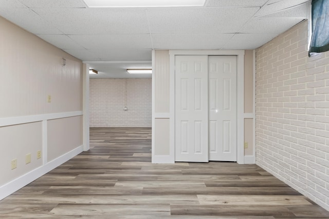 finished basement featuring brick wall, a drop ceiling, wood finished floors, and baseboards