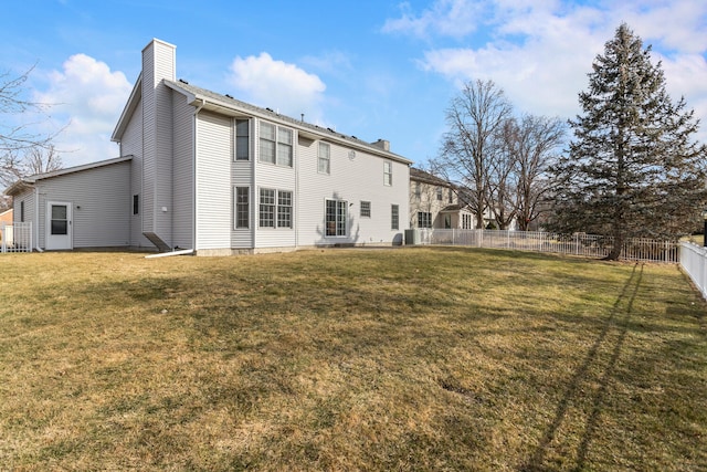 back of house with a fenced backyard, a lawn, and a chimney