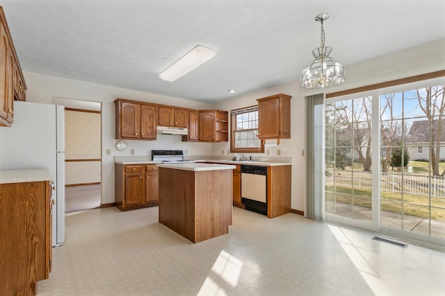 kitchen with under cabinet range hood, light countertops, a center island, dishwasher, and decorative light fixtures