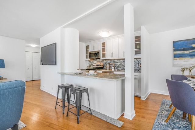 kitchen featuring white cabinets, backsplash, stainless steel appliances, light stone countertops, and light hardwood / wood-style flooring