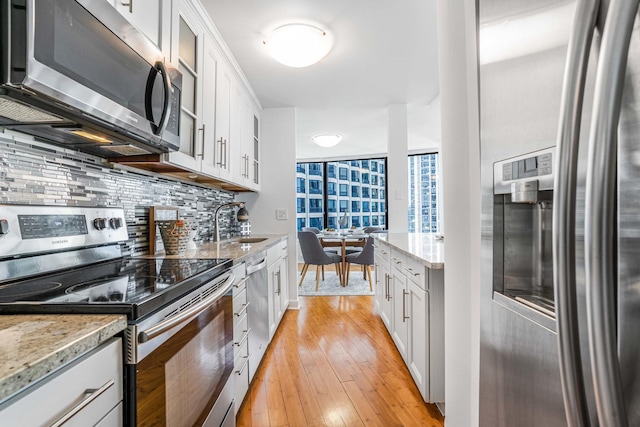 kitchen with white cabinetry, stainless steel appliances, light stone countertops, and decorative backsplash