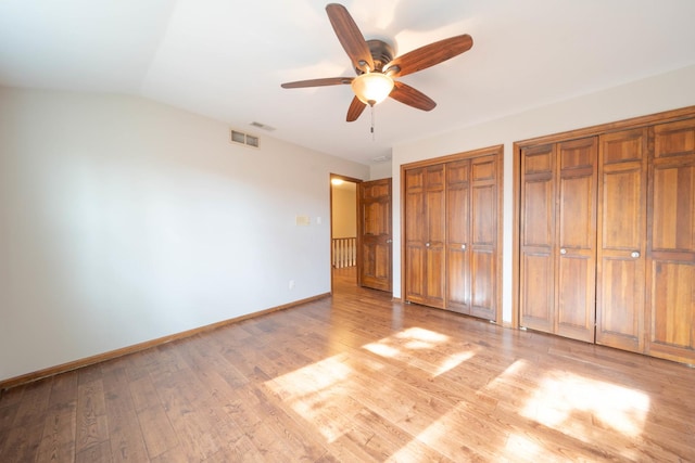 unfurnished bedroom with multiple closets, vaulted ceiling, ceiling fan, and light hardwood / wood-style flooring