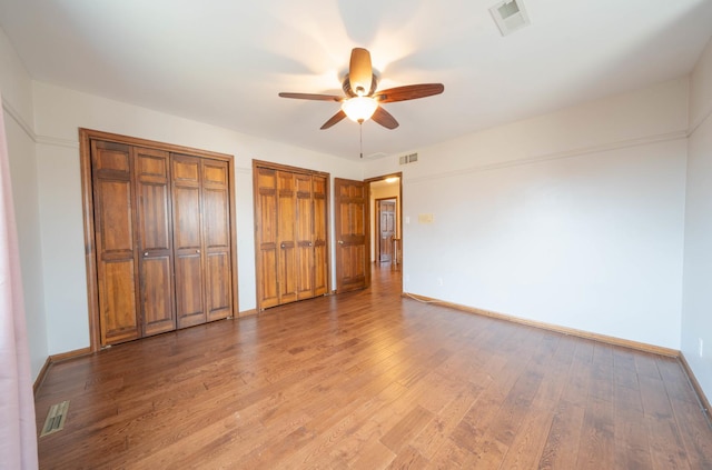 unfurnished bedroom with multiple closets, ceiling fan, and light hardwood / wood-style floors