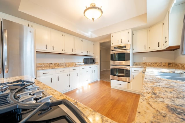 kitchen featuring appliances with stainless steel finishes, white cabinetry, light stone counters, light hardwood / wood-style floors, and a raised ceiling