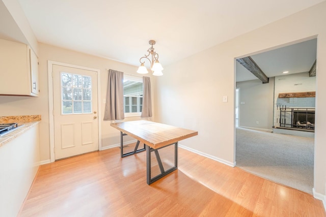 dining area featuring a large fireplace, a notable chandelier, beam ceiling, and light hardwood / wood-style flooring