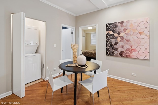 dining area featuring light wood finished floors, stacked washer and clothes dryer, crown molding, and baseboards