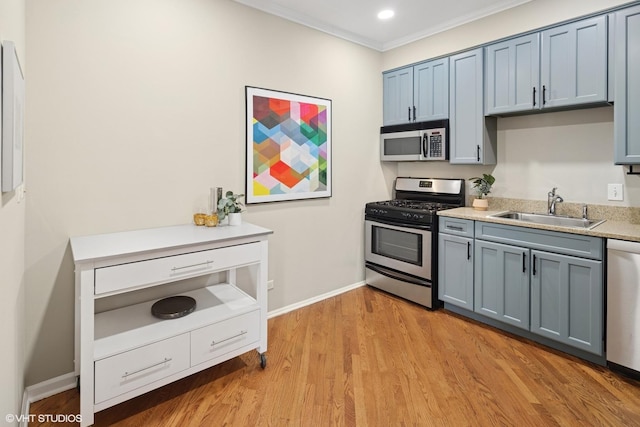 kitchen featuring light wood finished floors, ornamental molding, a sink, light countertops, and appliances with stainless steel finishes