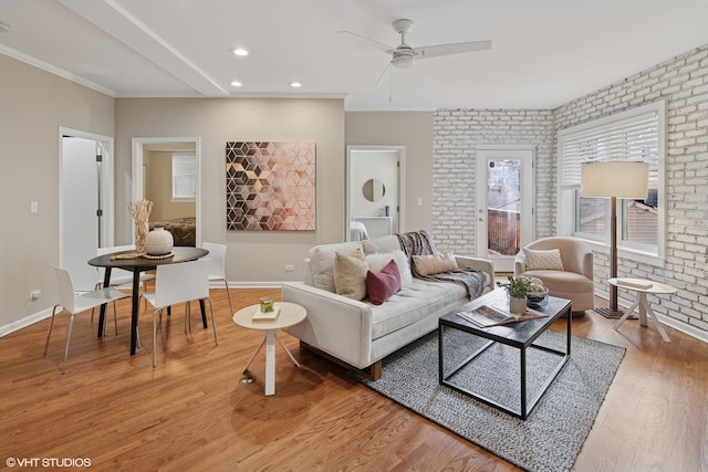 living room featuring baseboards, brick wall, crown molding, and light wood finished floors