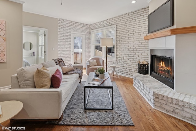 living room featuring a glass covered fireplace, crown molding, wood finished floors, and brick wall