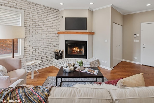 living area with ornamental molding, a fireplace, baseboards, and wood finished floors