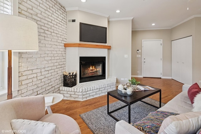 living room with visible vents, ornamental molding, a fireplace, and wood finished floors