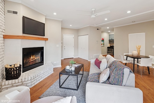 living area with wood finished floors, baseboards, visible vents, ornamental molding, and a glass covered fireplace