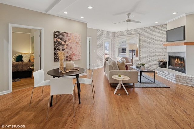 interior space with a fireplace, brick wall, a ceiling fan, and wood finished floors