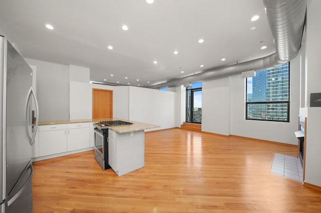 kitchen with light stone counters, light hardwood / wood-style flooring, appliances with stainless steel finishes, kitchen peninsula, and white cabinets