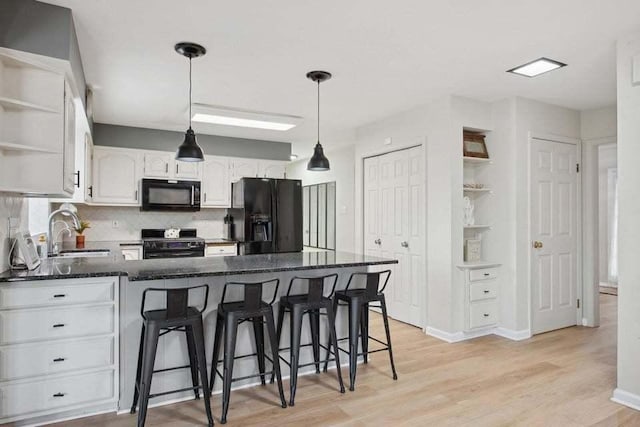 kitchen with sink, black appliances, a kitchen breakfast bar, light hardwood / wood-style floors, and white cabinets