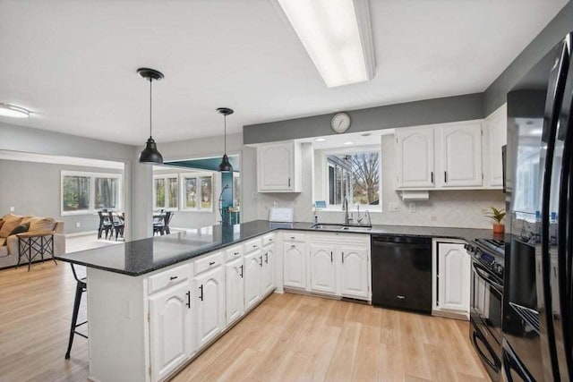 kitchen with black appliances, white cabinetry, a breakfast bar, and kitchen peninsula