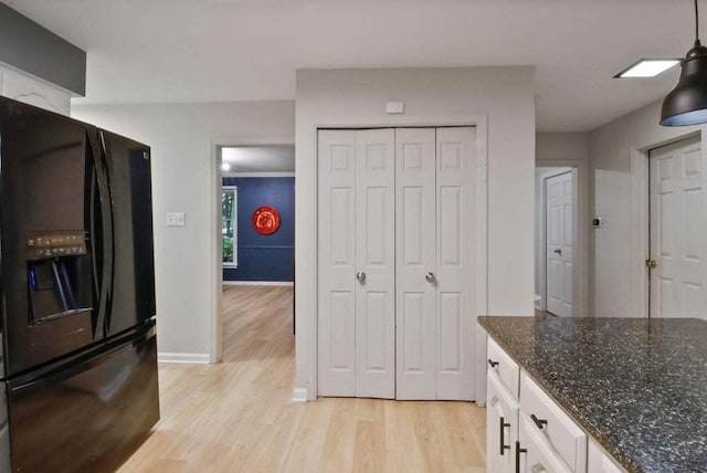 kitchen with white cabinetry, hanging light fixtures, dark stone countertops, light hardwood / wood-style floors, and black fridge with ice dispenser