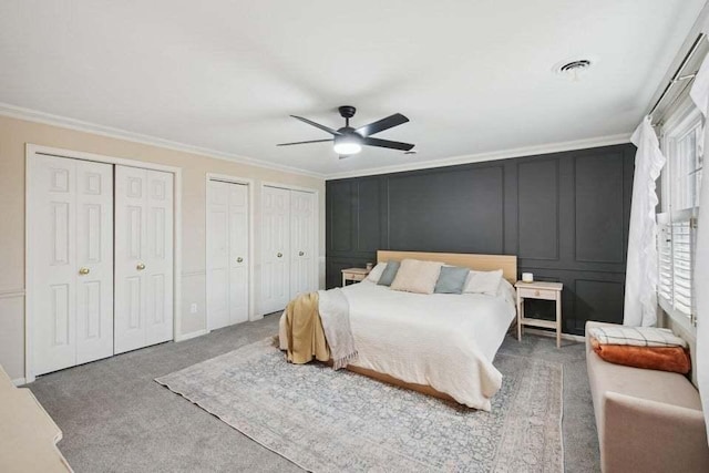 bedroom with ceiling fan, carpet floors, ornamental molding, and multiple closets