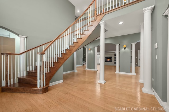 stairway featuring decorative columns, wood-type flooring, and a fireplace