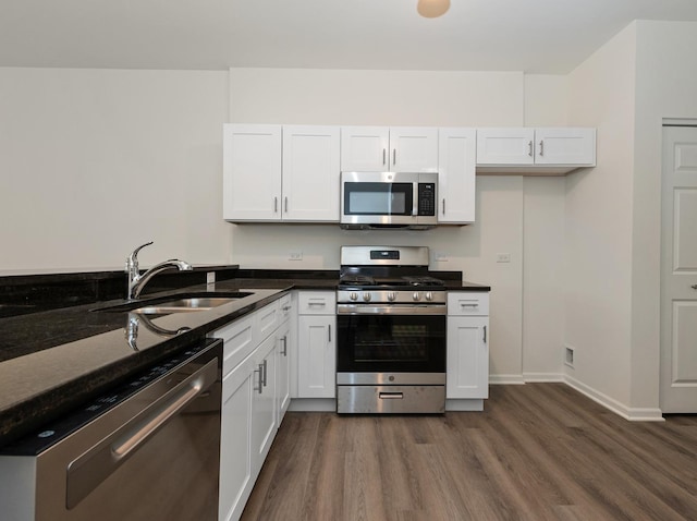 kitchen featuring appliances with stainless steel finishes, white cabinetry, sink, dark stone counters, and dark wood-type flooring