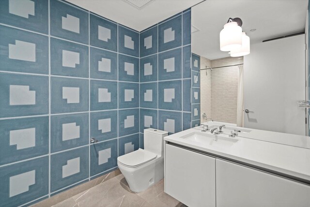 bathroom featuring tiled shower, toilet, tile walls, vanity, and tile patterned flooring