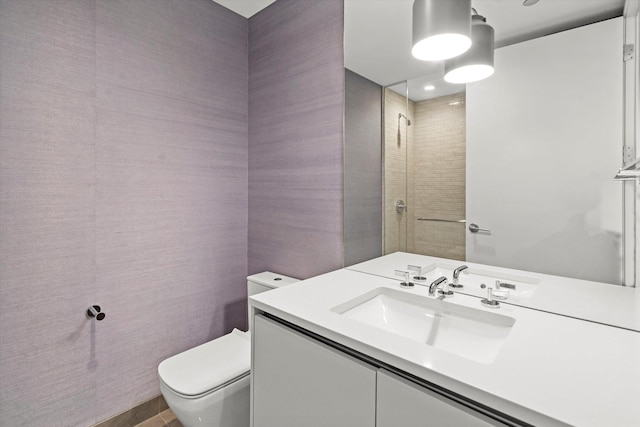 bathroom with vanity, tiled shower, and toilet