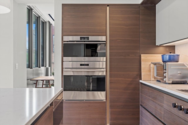 kitchen featuring white cabinetry, stainless steel double oven, and light stone counters