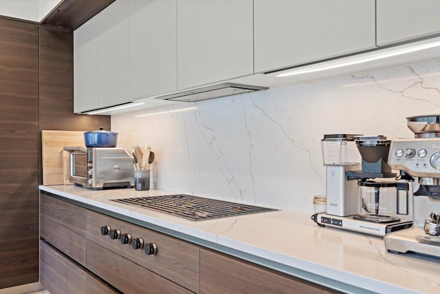 kitchen featuring tasteful backsplash, light stone counters, and white cabinets