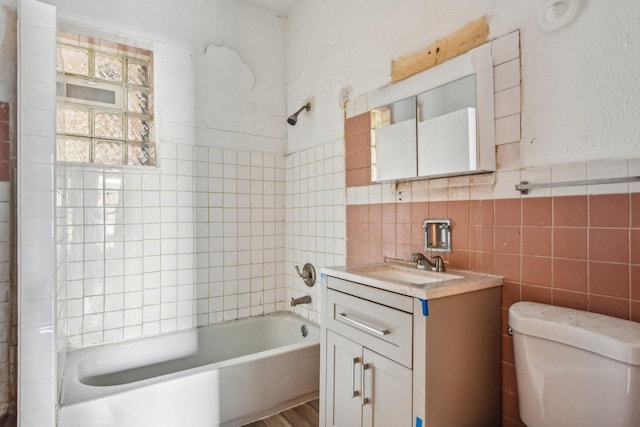 full bathroom featuring tile walls, vanity, tiled shower / bath, and toilet