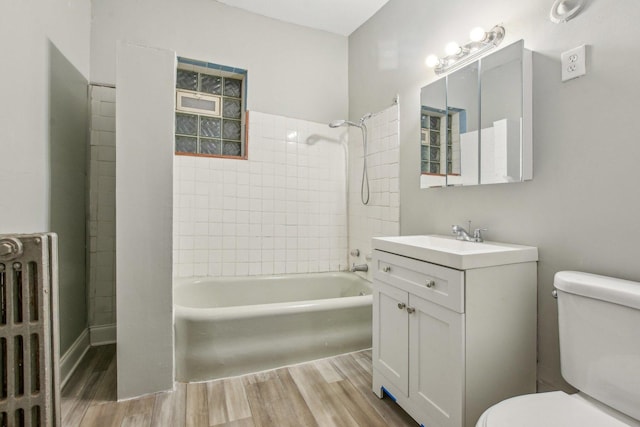 full bathroom featuring hardwood / wood-style floors, tiled shower / bath combo, radiator heating unit, vanity, and toilet