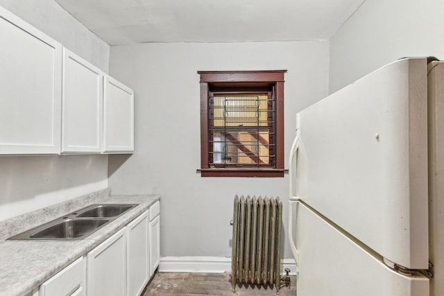 kitchen featuring sink, white cabinetry, radiator heating unit, white fridge, and light wood-type flooring