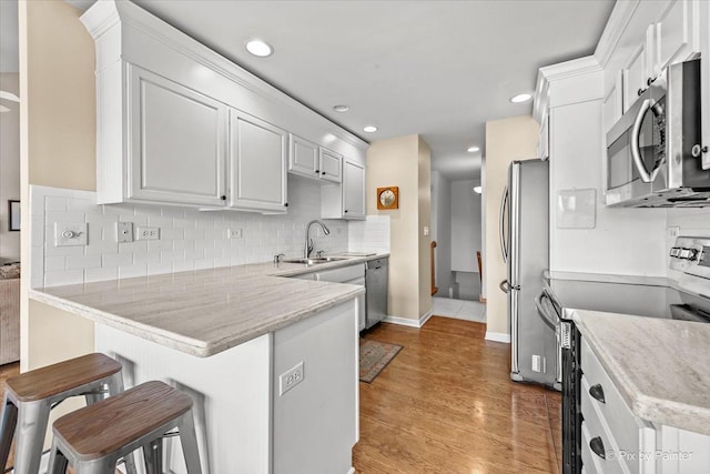 kitchen with sink, appliances with stainless steel finishes, a kitchen breakfast bar, white cabinets, and kitchen peninsula