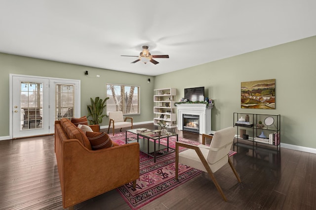 living area featuring dark wood-style floors, a glass covered fireplace, ceiling fan, and baseboards