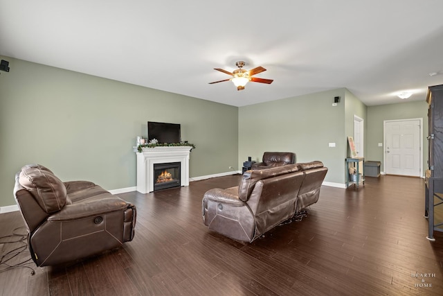 living room featuring ceiling fan, baseboards, dark wood-type flooring, and a glass covered fireplace