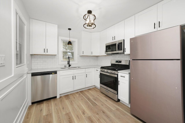 kitchen with appliances with stainless steel finishes, white cabinetry, sink, hanging light fixtures, and light wood-type flooring