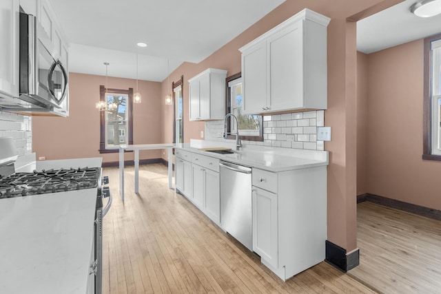 kitchen featuring pendant lighting, sink, appliances with stainless steel finishes, light hardwood / wood-style floors, and white cabinets