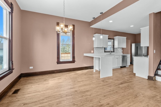 kitchen with white cabinetry, light wood-type flooring, appliances with stainless steel finishes, pendant lighting, and decorative backsplash